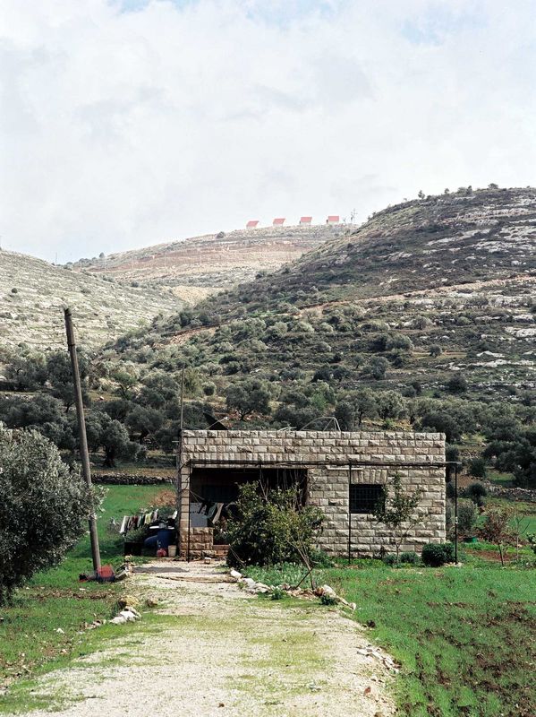 Two mountains with Israeli settlements and a Palestinian house in the foreground
